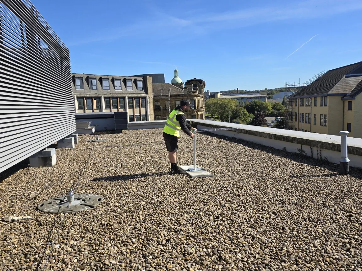 Engineer installing a weighted flat-roof TV aerial mount on a large Bradford shopping-centre roof