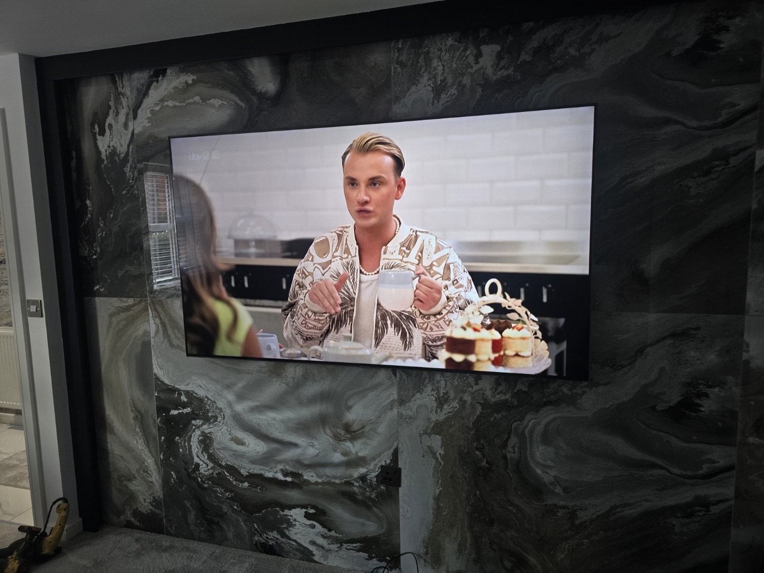 75-inch television mounted on a black and grey patterned porcelain-tiled feature wall in a Preston home.